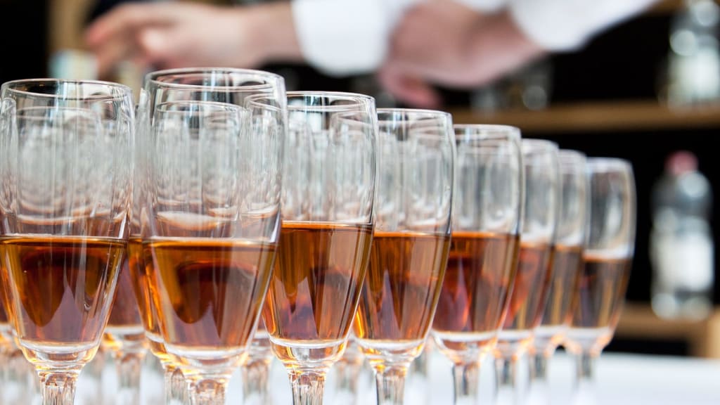 A row of filled wine glasses arranged in a line, with a person in the background reaching out towards them, demonstrating the importance of understanding the various types of liquor licenses in California.